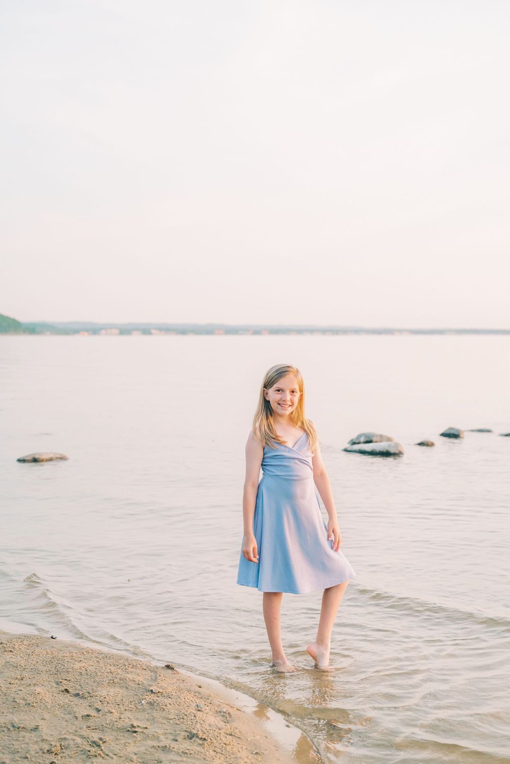 Figure in blue dress standing ankle-deep in calm waters at sunset.