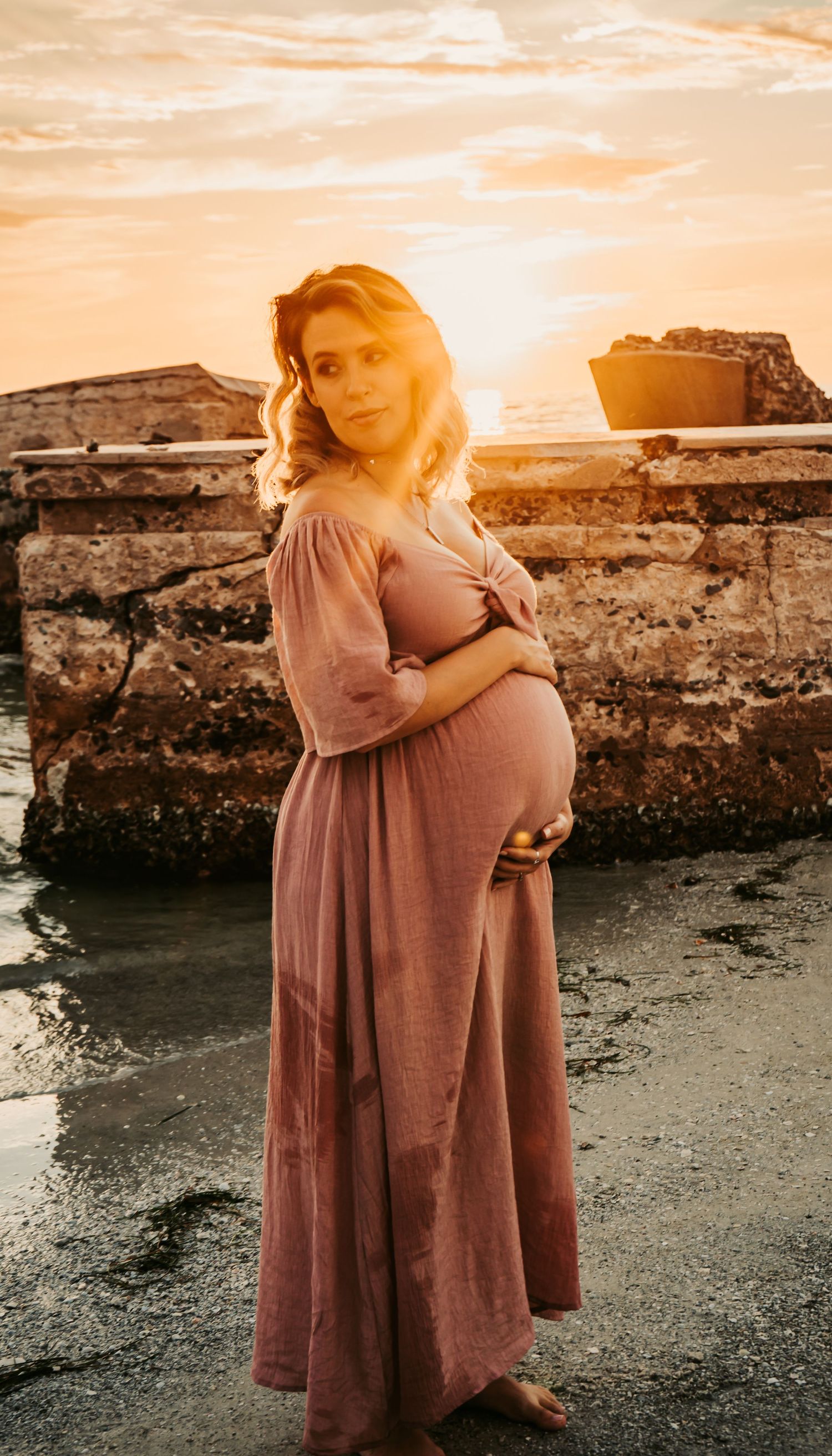 Outdoor Maternity Session at Ft. Desoto in St. Pete, FL; woman embracing her pregnancy belly near ruins at sunset
