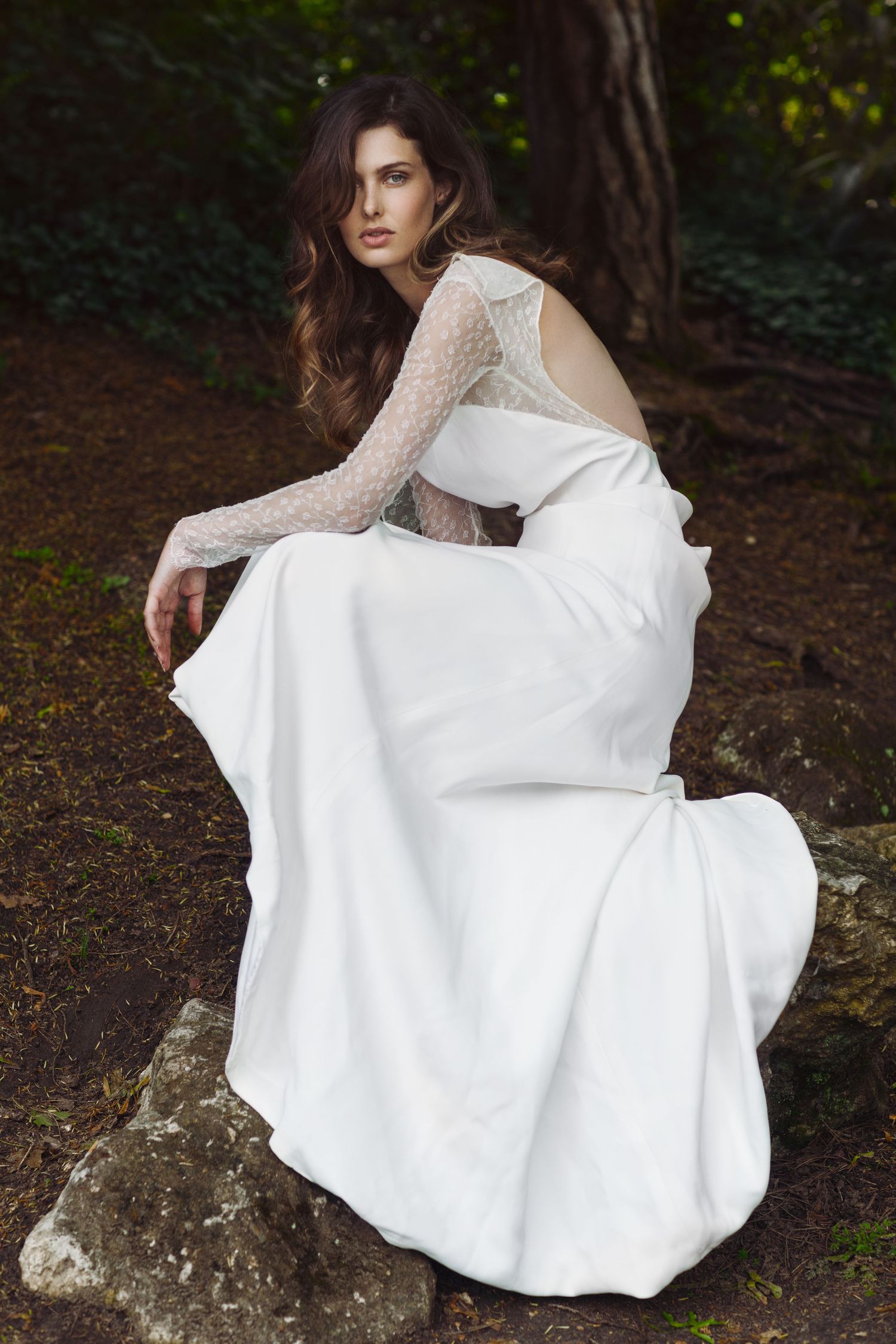 Elegant bridal portrait featuring long-sleeved lace wedding dress on mossy forest ground.