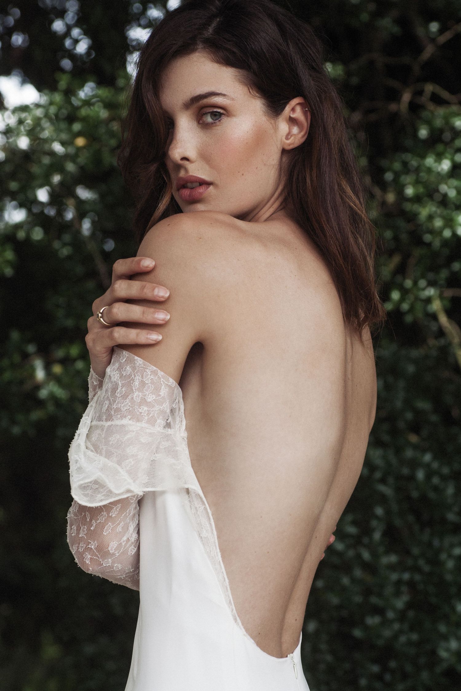 Backless wedding dress with delicate lace sleeves shown in intimate bridal portrait.