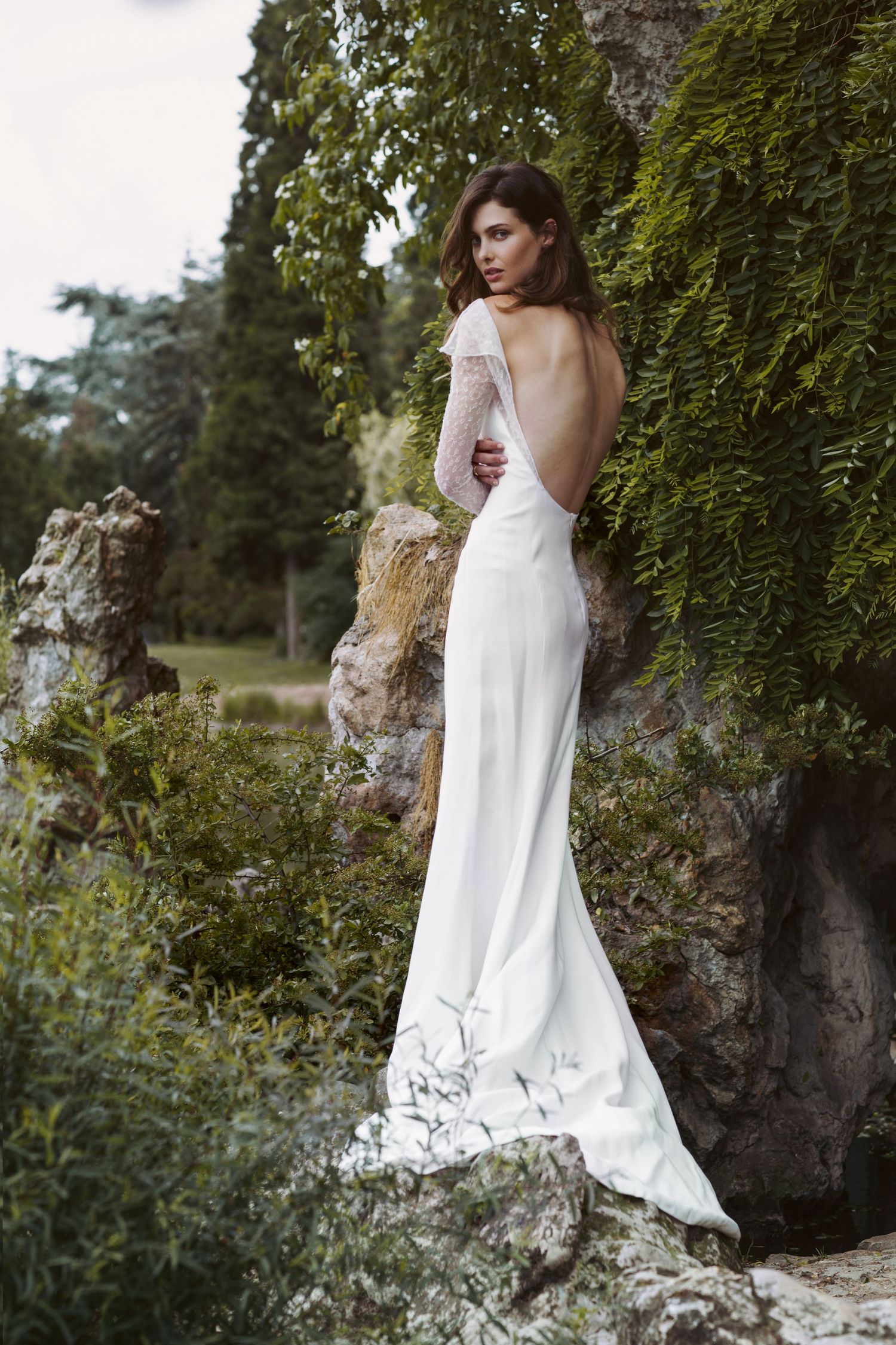 Sleek white wedding gown with open back photographed against ivy-covered stone wall.