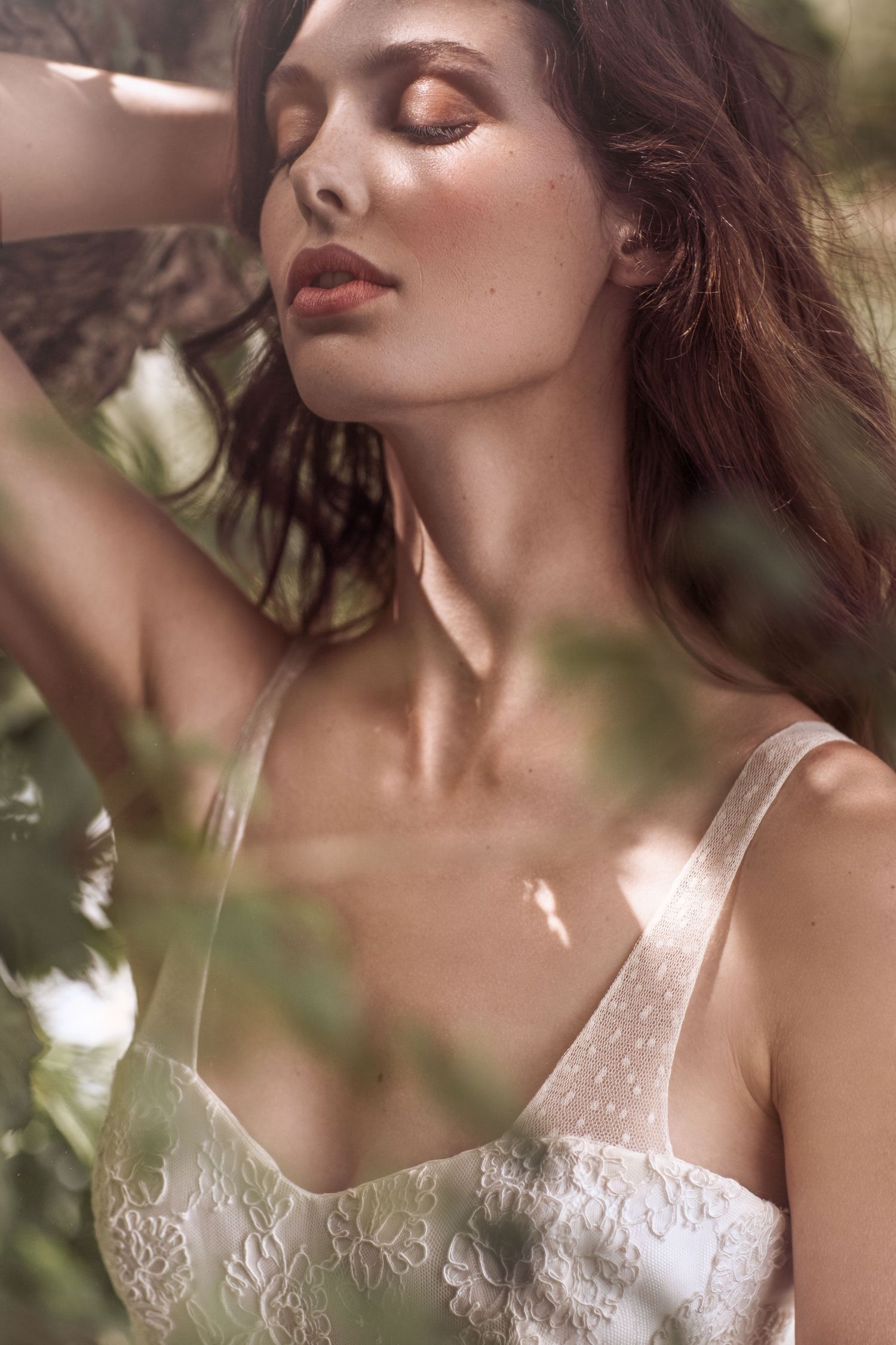 Dreamy bridal portrait with soft lighting and lace details through leaves.