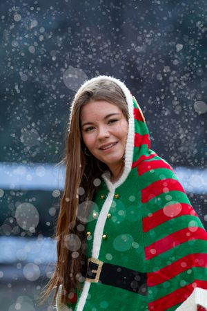 Person wearing festive red and green striped Christmas outfit in falling snow.