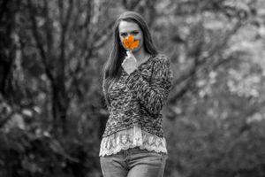 Person in patterned top holding orange flower in black and white selective color photo.
