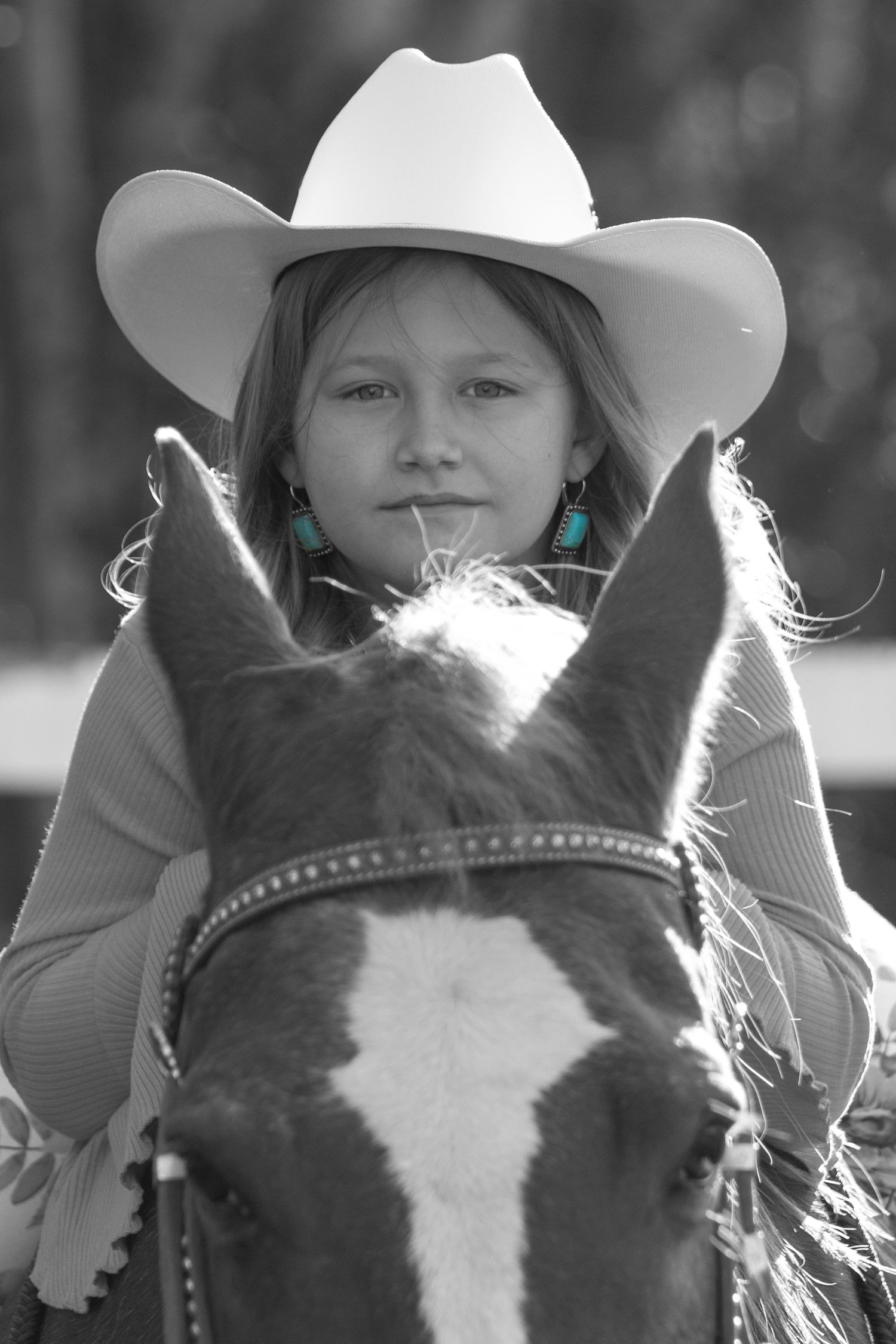 Black and white portrait of someone in cowboy hat sitting atop horse with turquoise earrings.