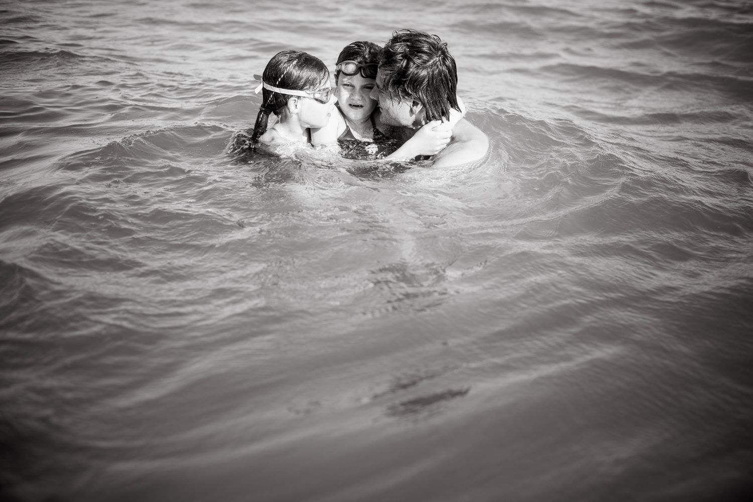 Father holding two of his girls on his hands in the water at Marbella beach.