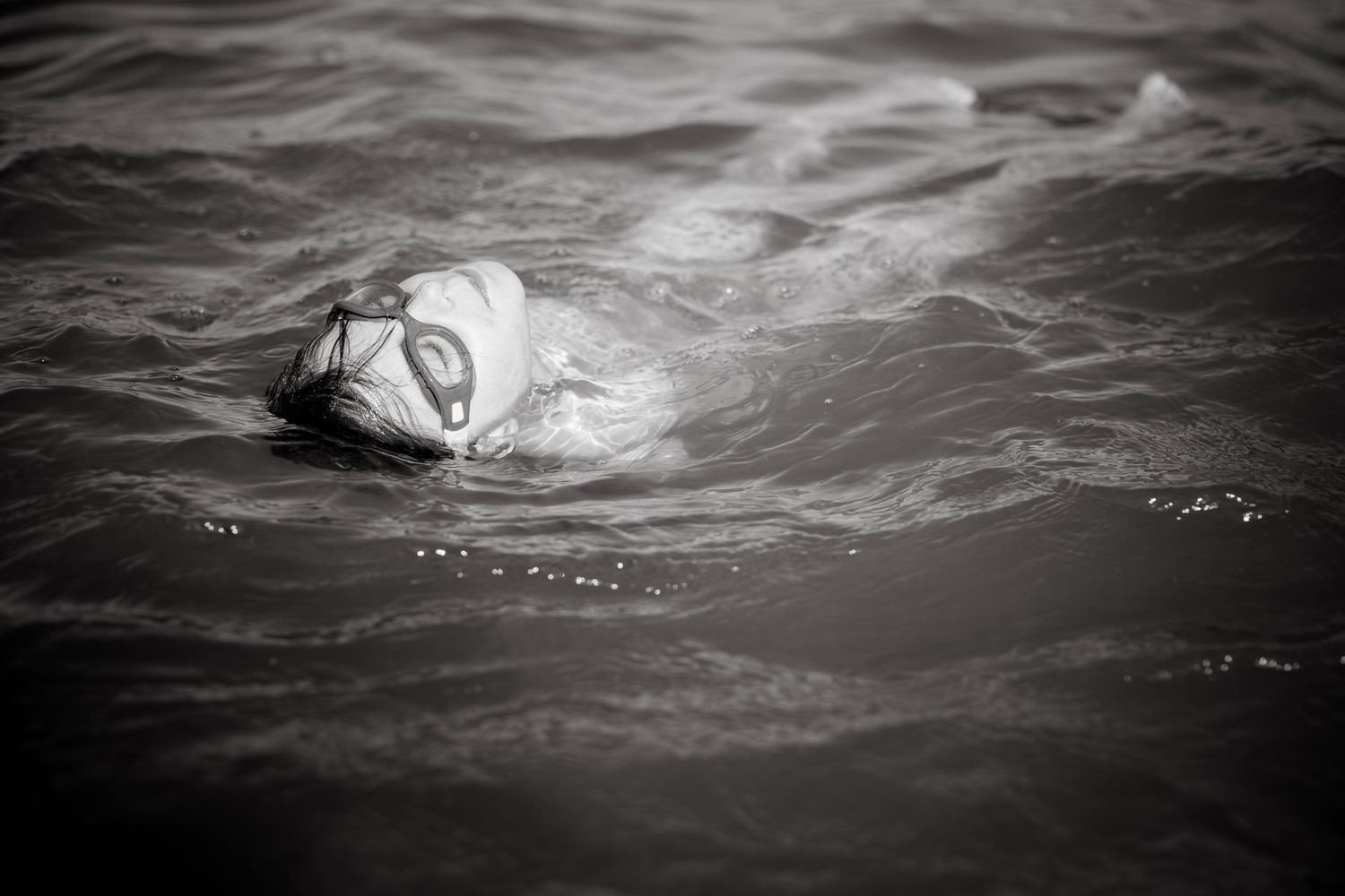 Girl swim on her back with swim googles at Marbella beach.