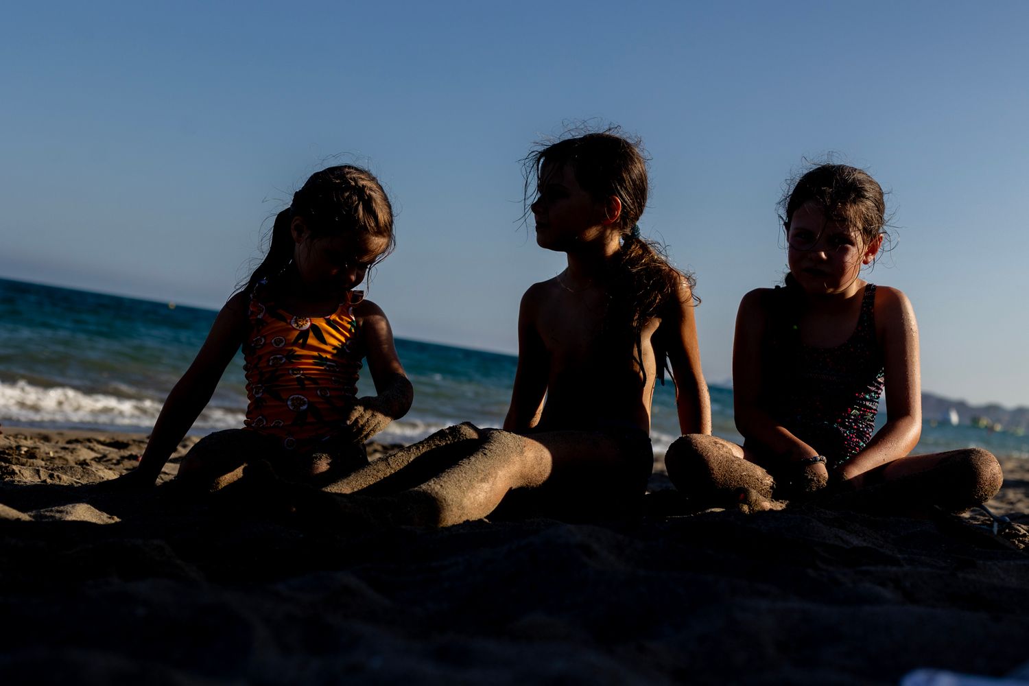 ChatGPT Plus
Three girls sit in the sand at the beach during golden hour, their silhouettes softly lit against the fading sunlight and ocean