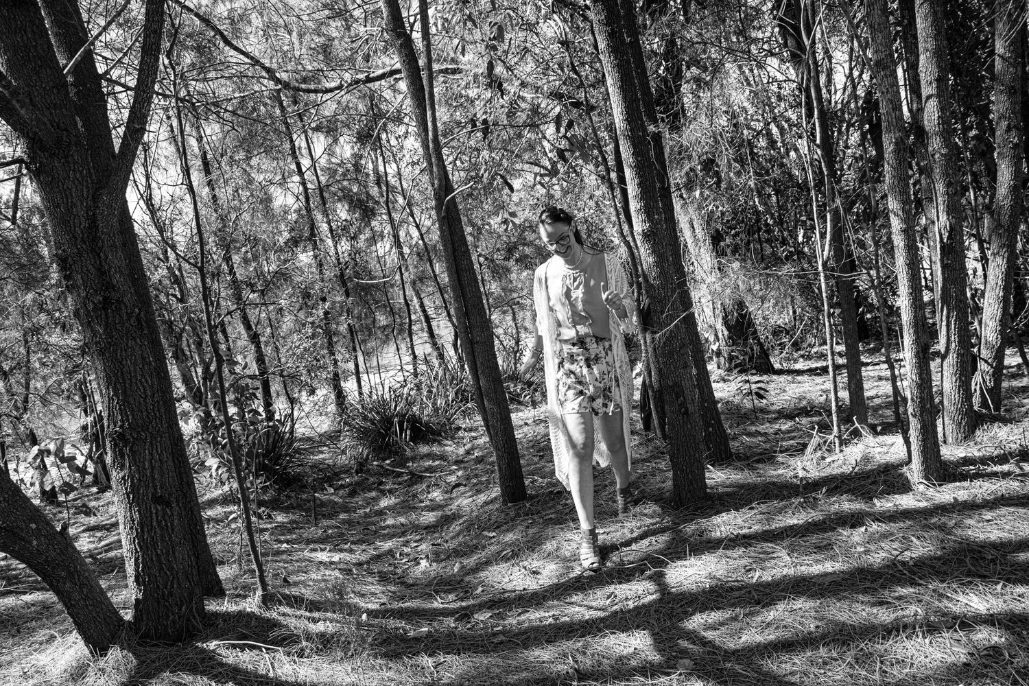 Black and white photo of figure walking through sunlit wooded path.