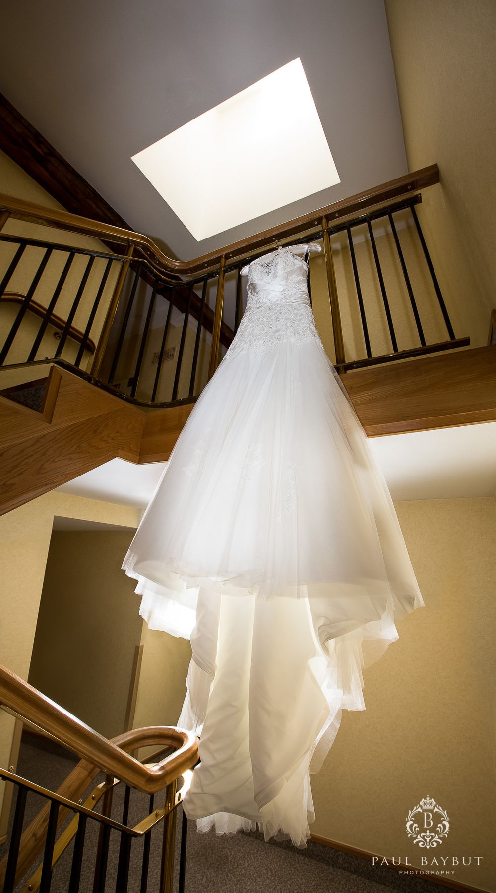 White wedding dress hanging from a skylight in dramatic lighting on wooden staircase.