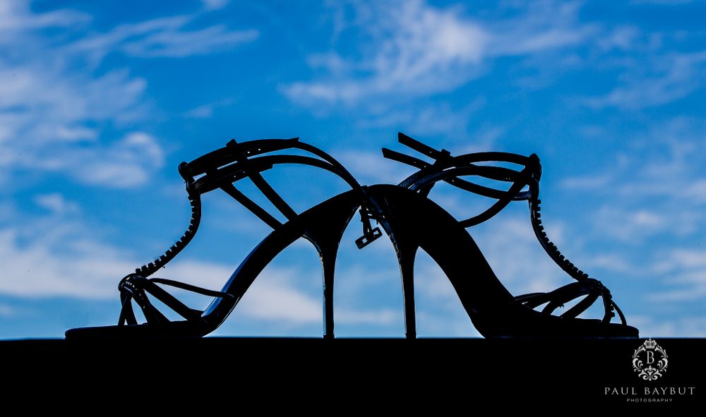 Silhouette of elegant high heel wedding shoes against blue sky background.
