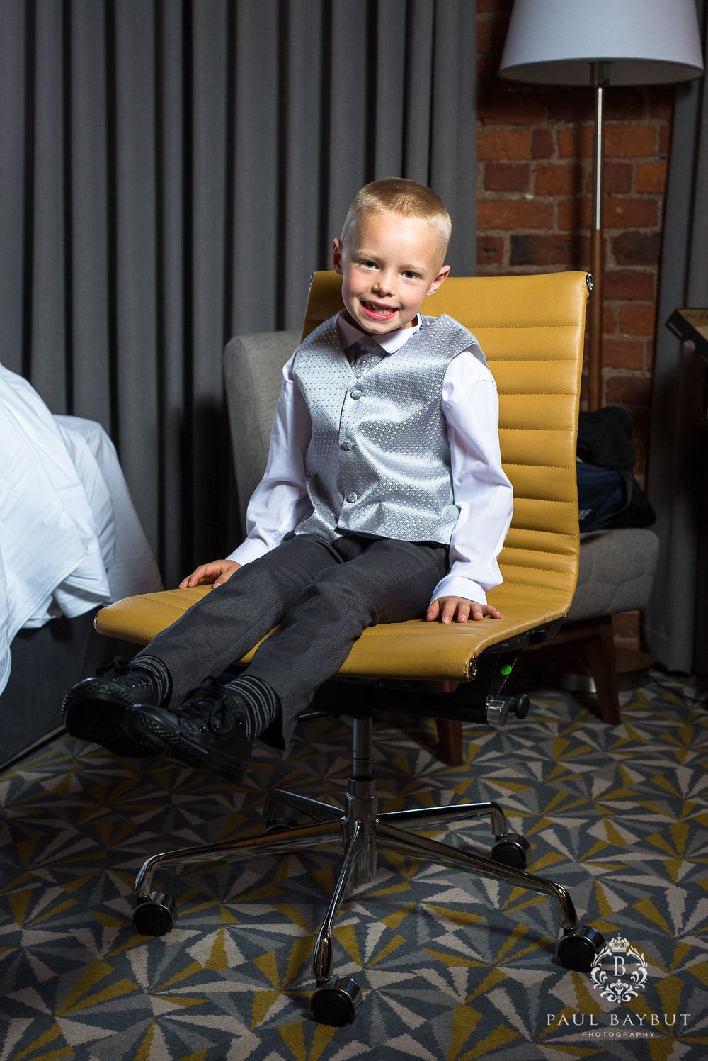 Child in formal wear sitting on yellow office chair with playful expression.