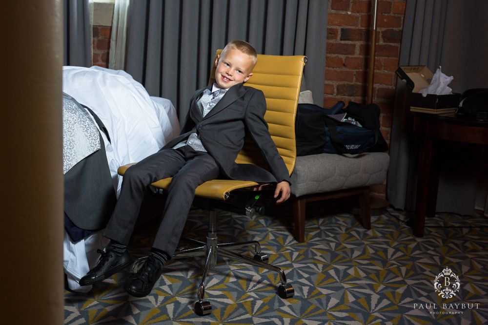 A young boy in a formal suit relaxes on a yellow chair in a hotel room.