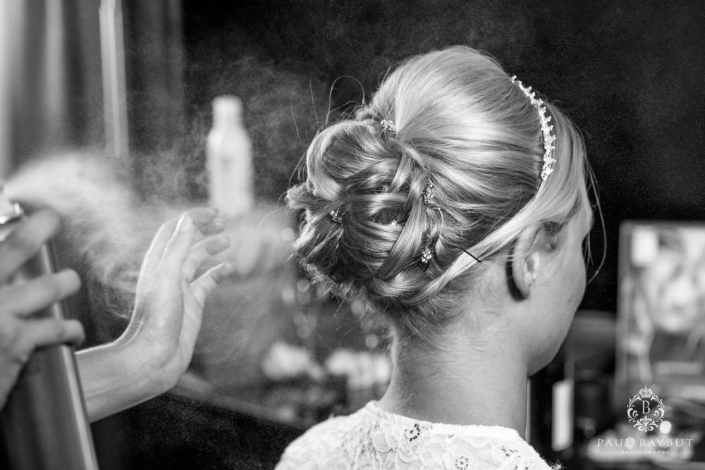 A black and white close-up of a bride's elegant updo with decorative hairpiece being styled.