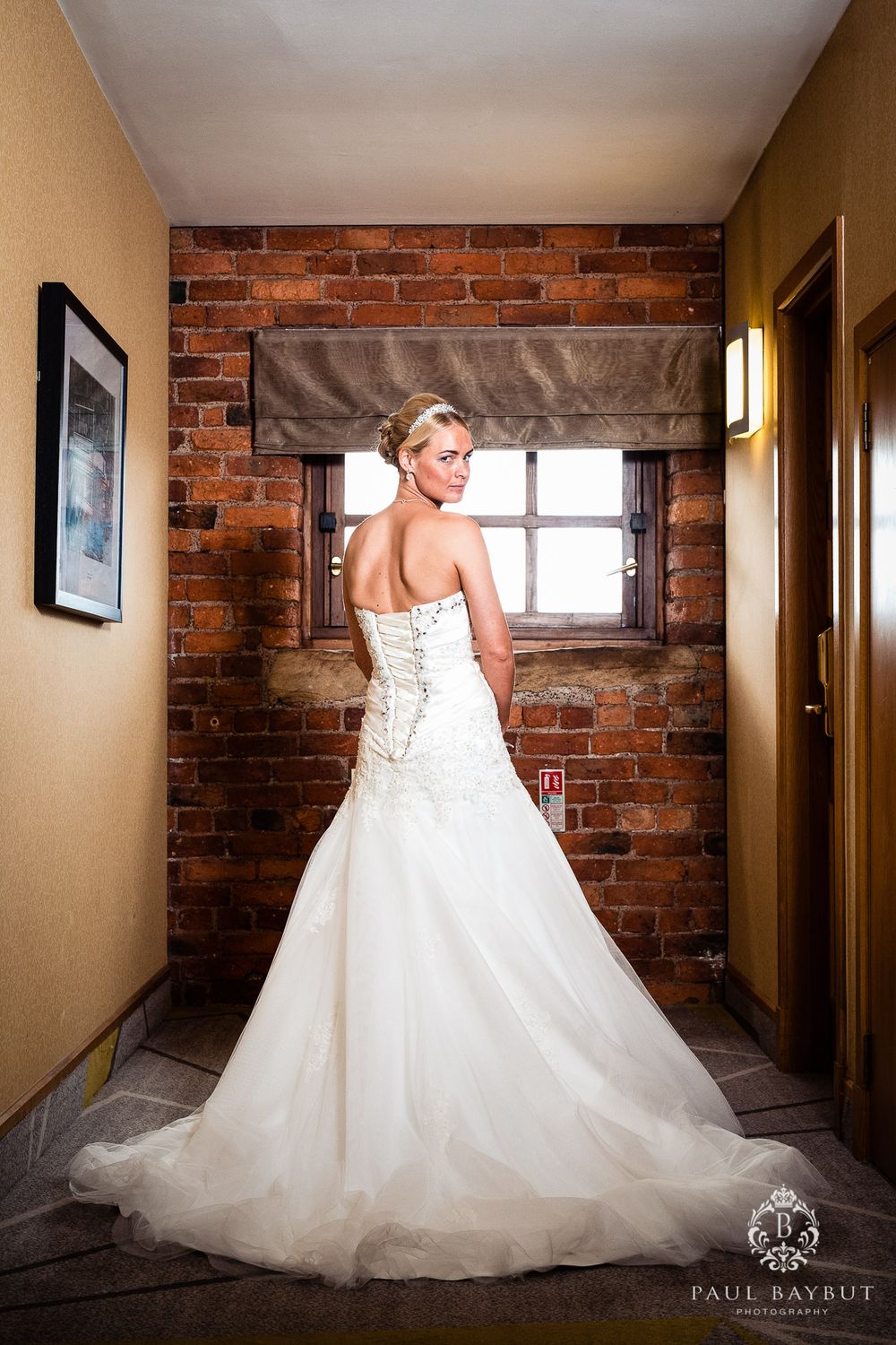 Elegant bridal portrait showing detailed back of wedding gown against exposed brick wall.