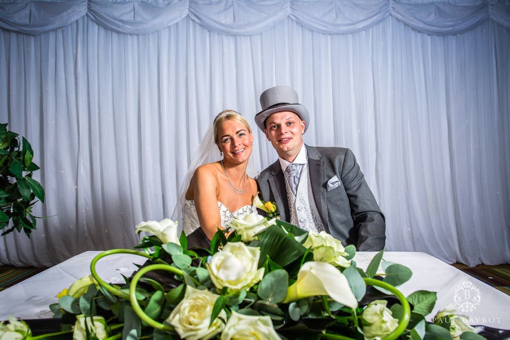 Newlyweds pose behind elegant white and green floral arrangements at their reception.