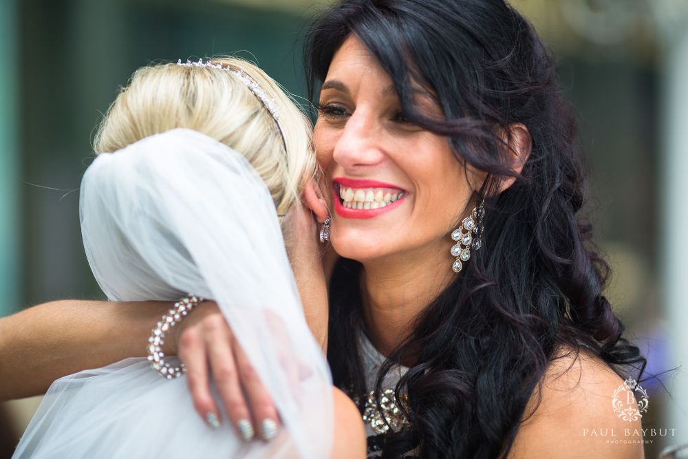 Two wedding guests share an emotional embrace while wearing formal attire.