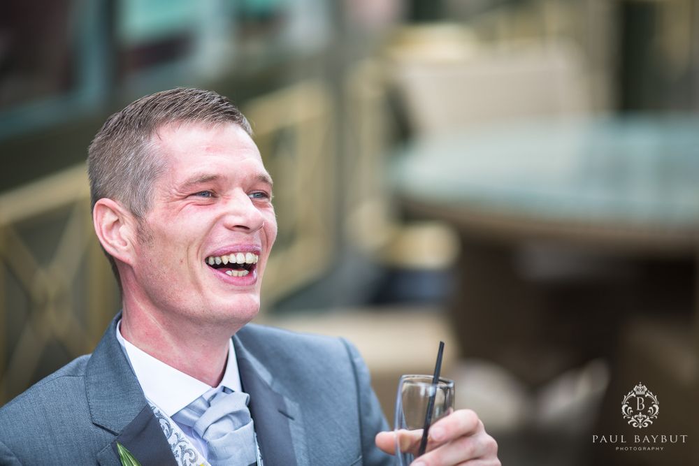 A guest in a grey suit laughs heartily during a wedding celebration.