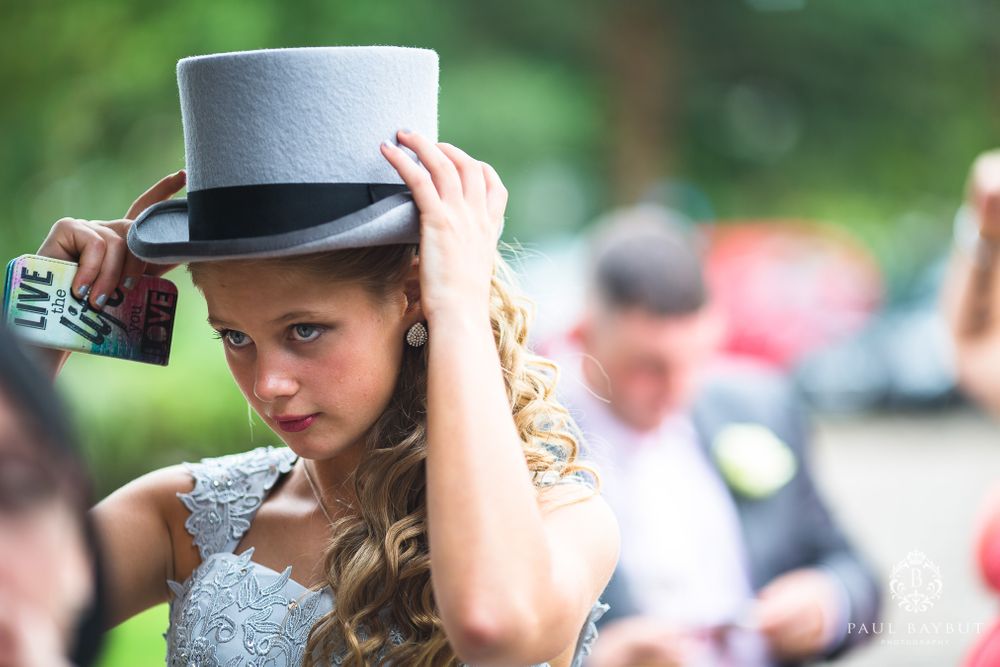 A stylish guest adjusts their top hat while wearing an elegant silver dress.