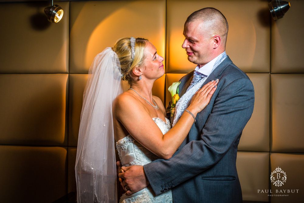 A bride in white dress and groom in gray suit share an intimate moment during their wedding.