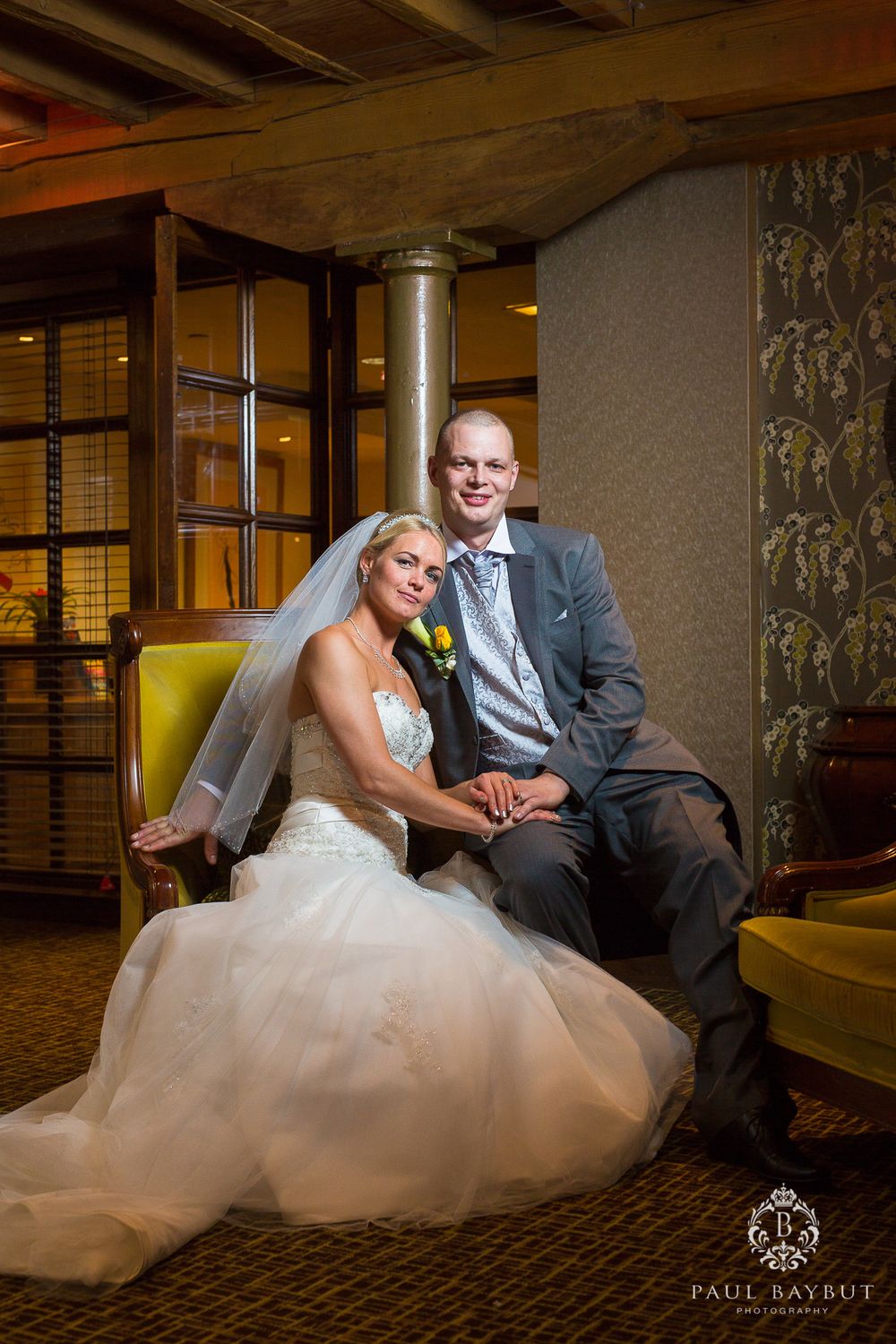 A wedding couple poses together on a yellow couch in an elegantly decorated indoor setting.