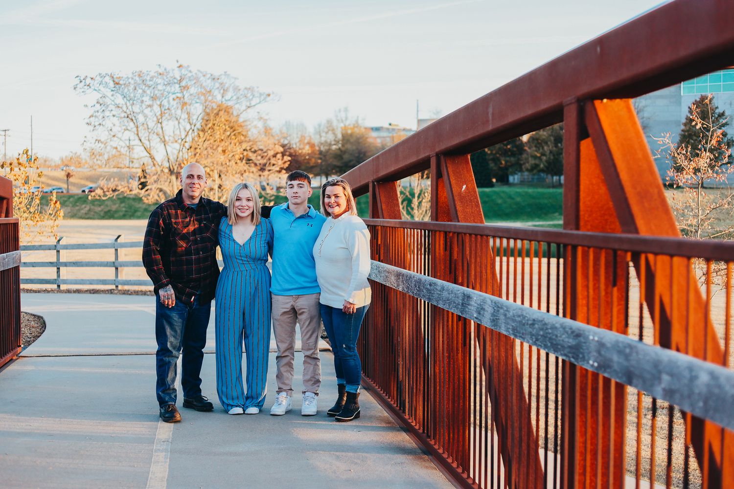 People stand together for a photo on a rustic red metal bridge with wooden railings in an autumn park setting.