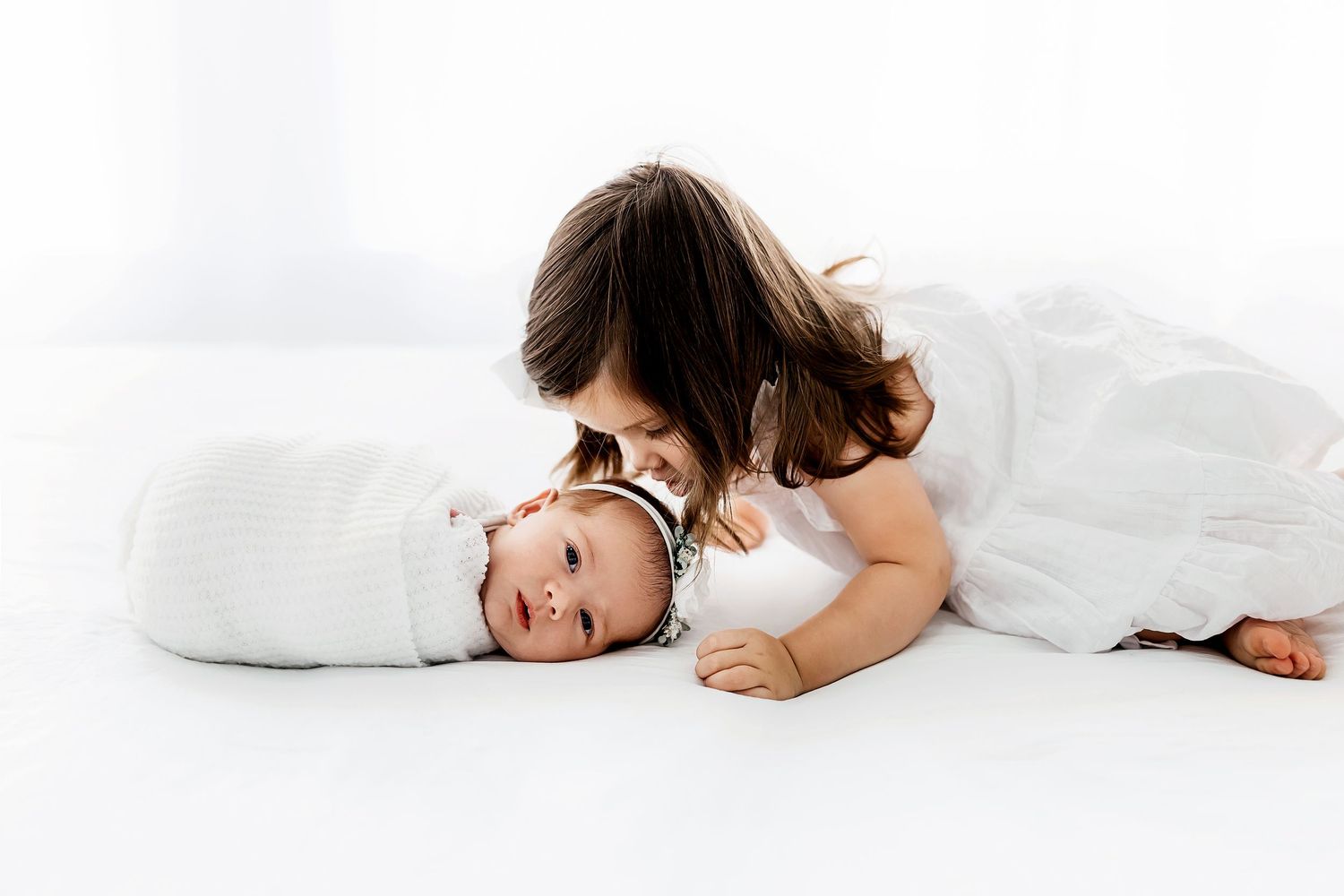 Sleeping infant wrapped in soft white swaddle on white blanket.