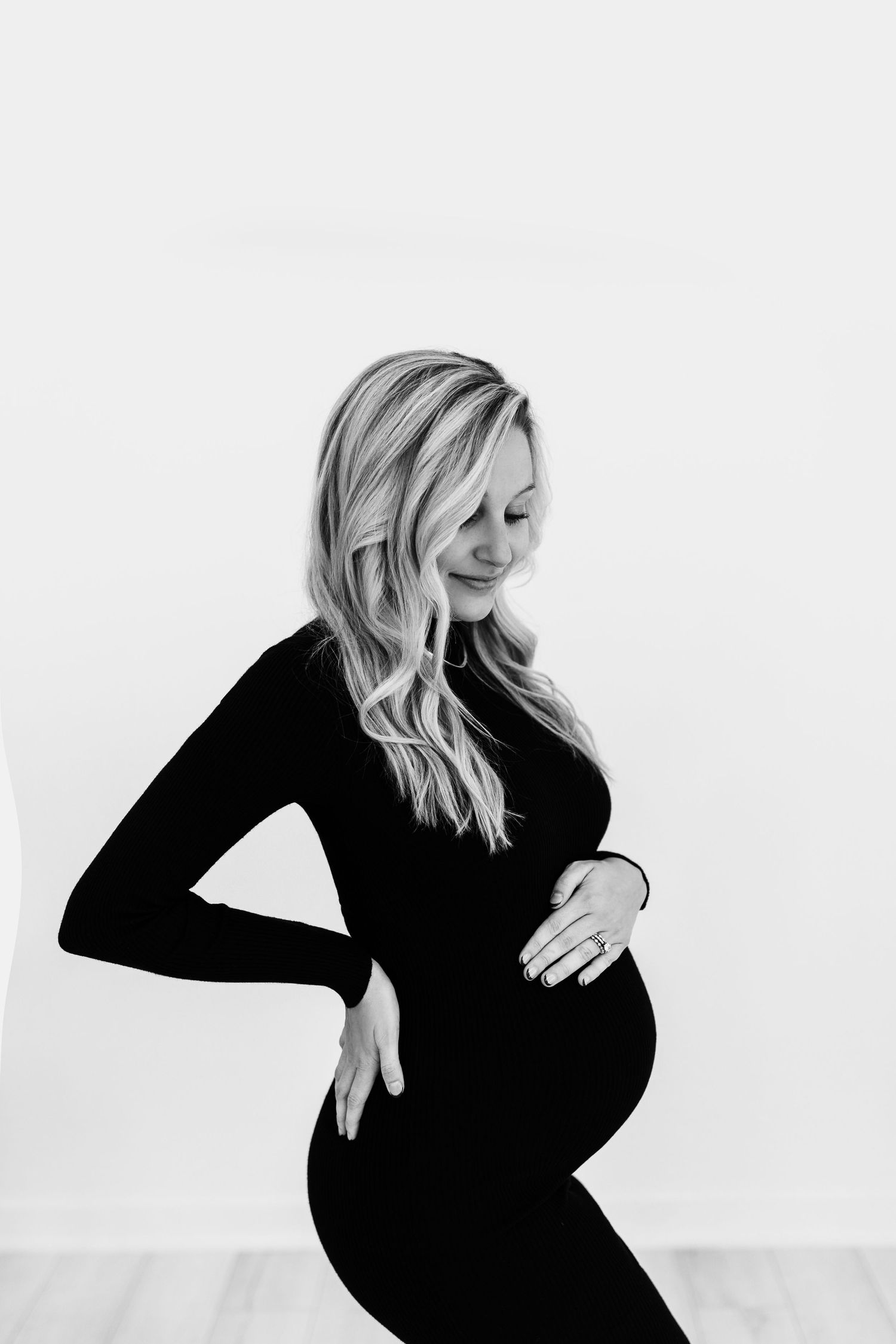 Black and white portrait showcasing an elegant maternity pose against a minimal background.
