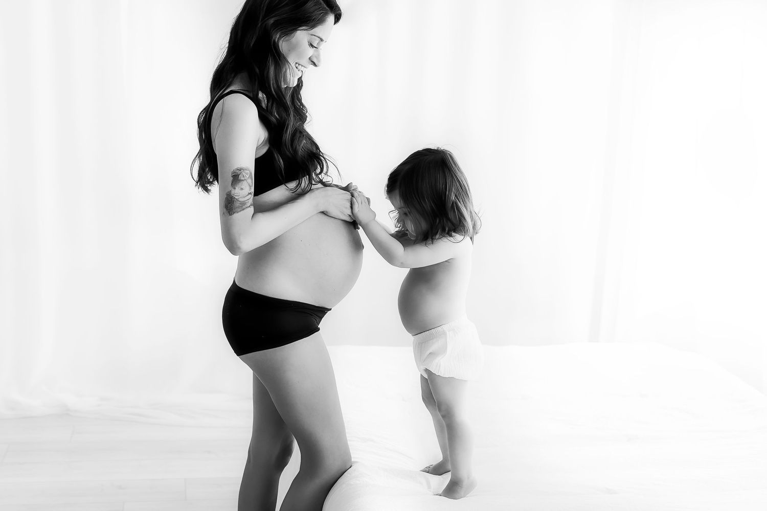 Black and white image of pregnant woman and small child touching belly.