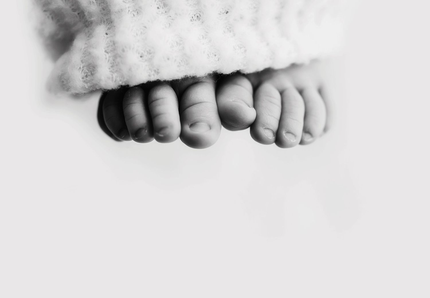 Close-up black and white photo of tiny baby toes peeking under blanket.
