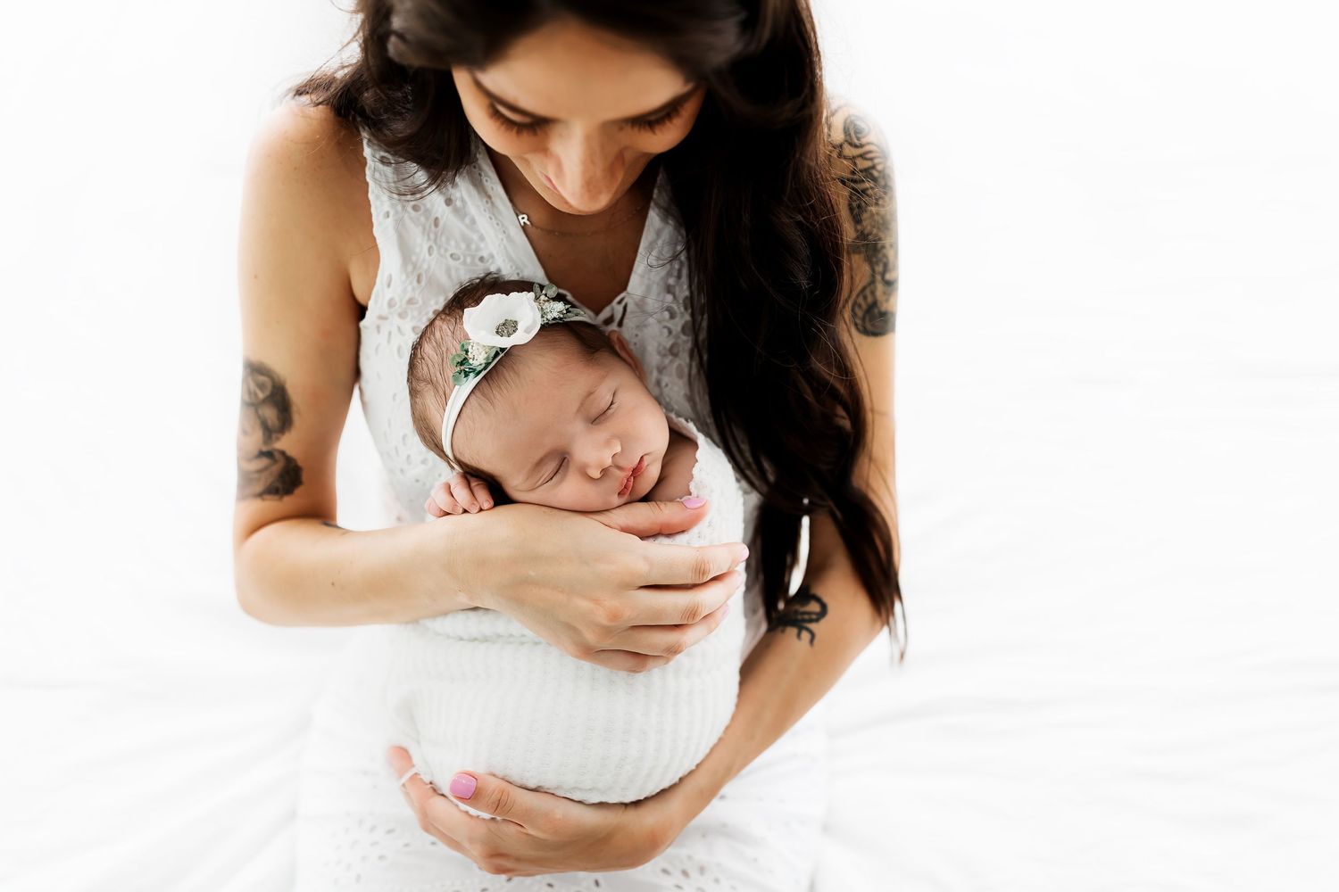Newborn wrapped in white blanket being held against white backdrop.