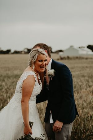 bride laughing in white lace wedding dress with groom behind laughing