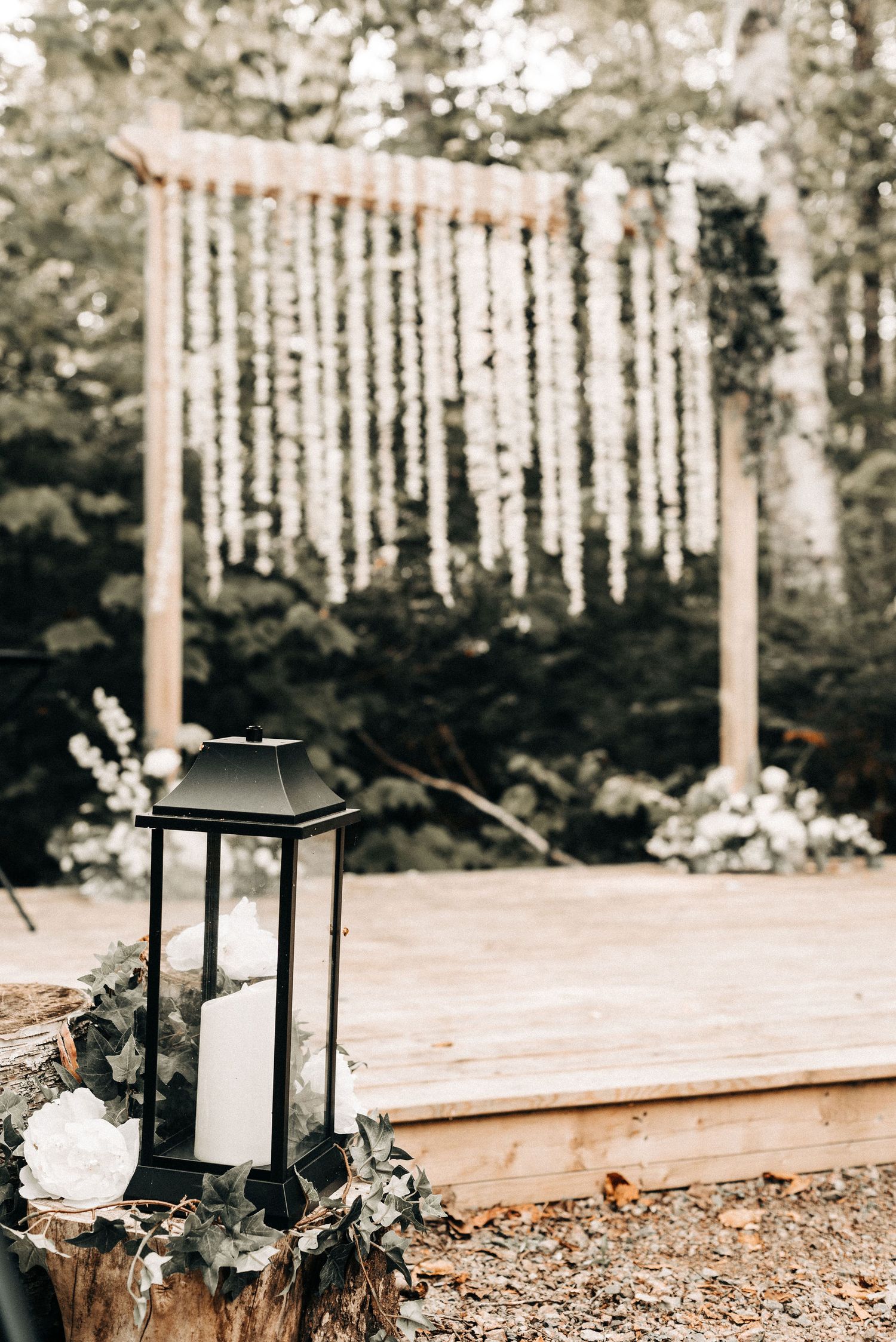 Black lantern decoration beside a hanging floral backdrop at an outdoor wedding venue.