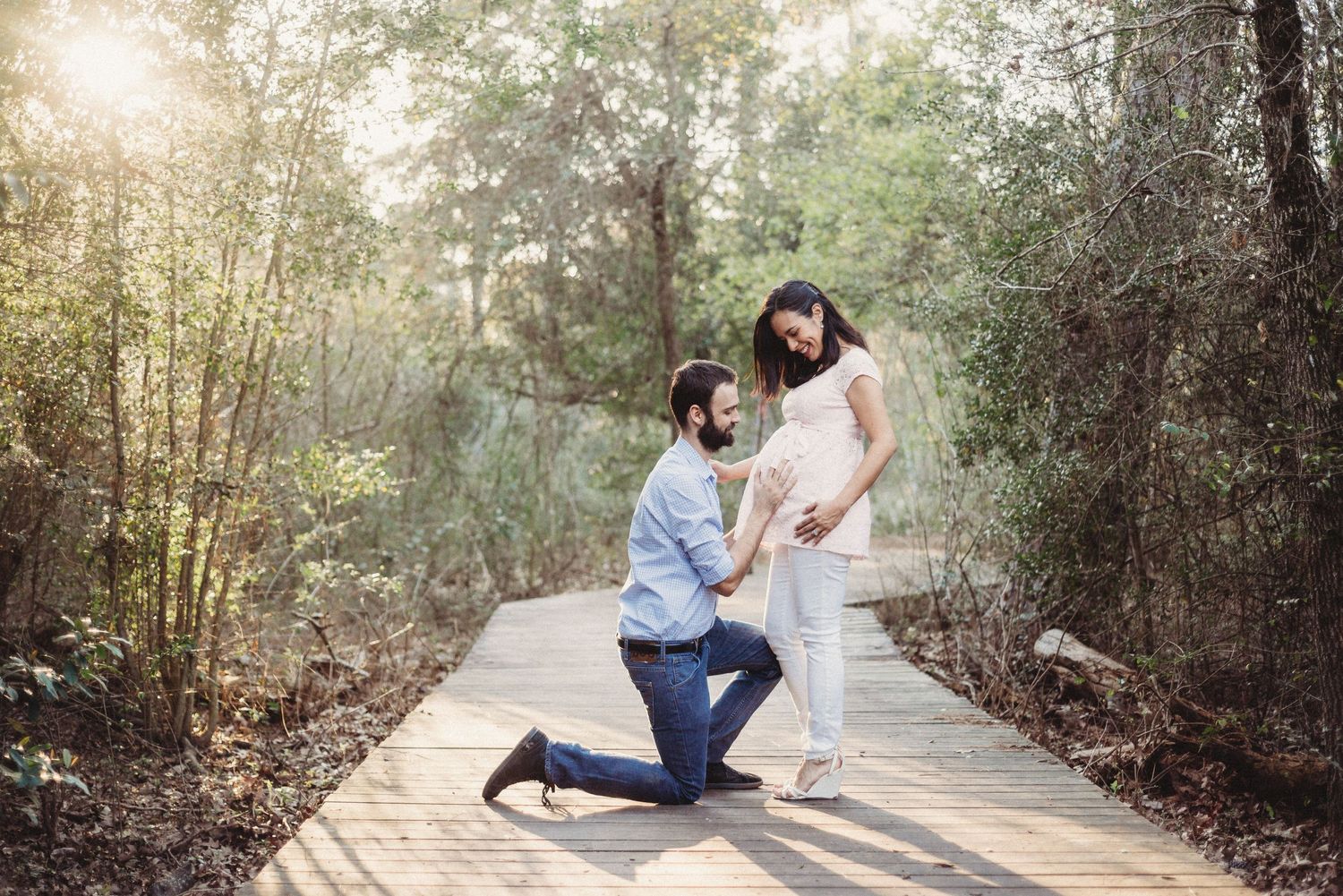Romantic couple poses along a tree-lined pathway during engagement photo session at sunset.