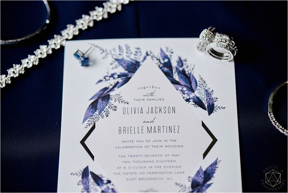 Elegant wedding invitation with blue watercolor feathers and jewelry details on navy background.