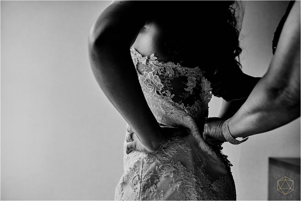 Black and white close-up of a wedding dress being laced up in dramatic lighting.