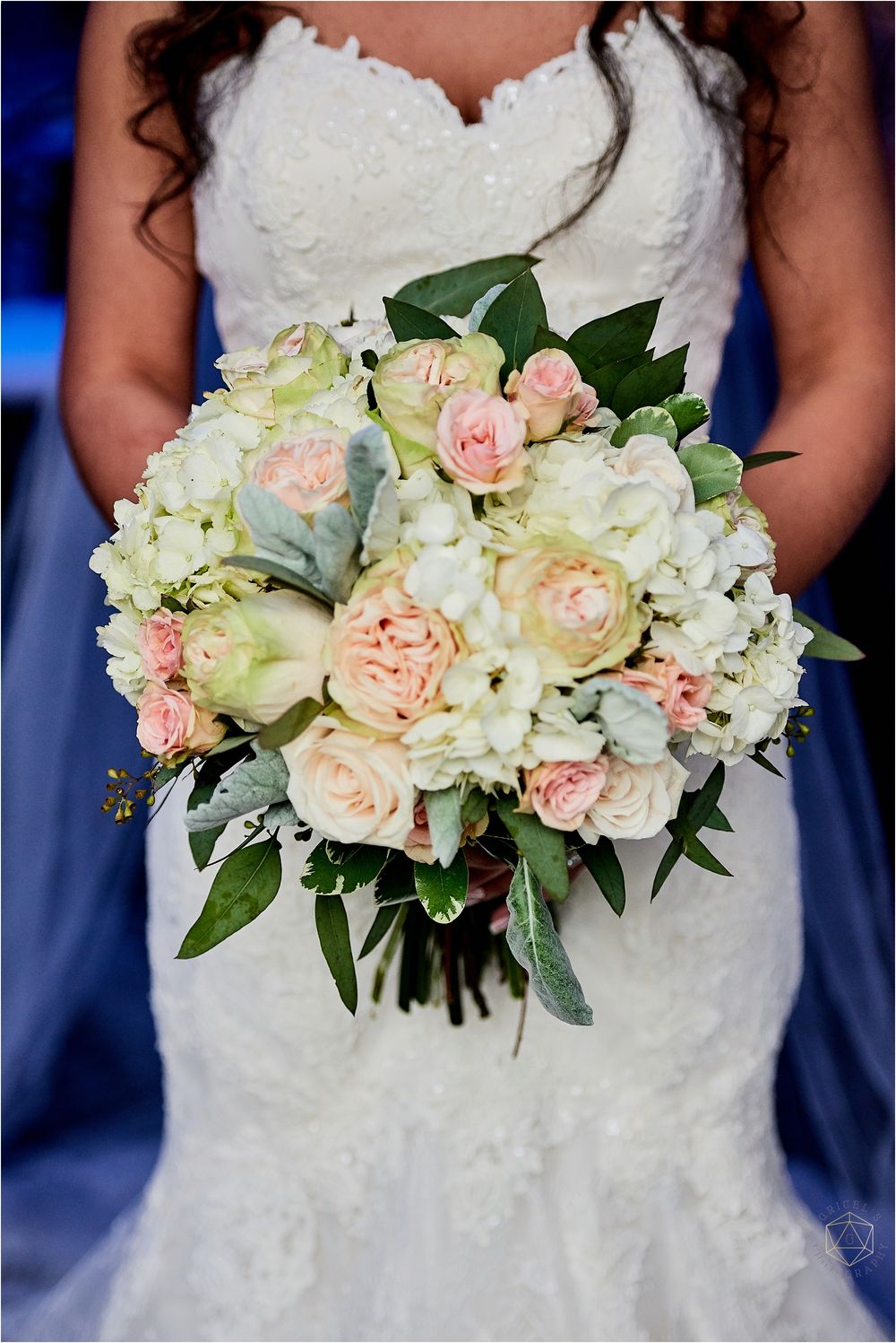 Detailed shot of wedding bouquet with blush roses and white hydrangeas against blue background.