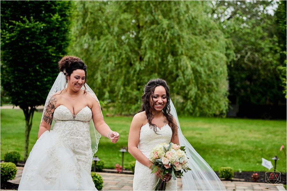 Two brides sharing a joyful moment in their wedding dresses outdoors.