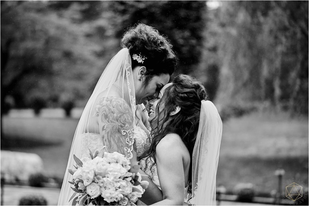 Black and white photo of two brides sharing an intimate moment in a garden setting.