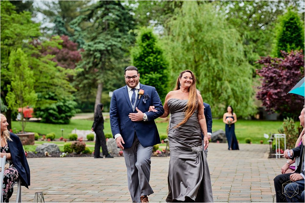 Wedding party members process down a stone walkway in formal attire.