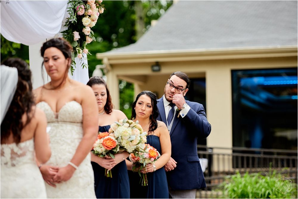 Wedding party members in navy and white attire gather during outdoor ceremony.