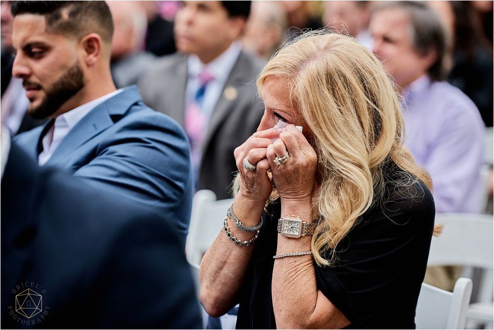 An emotional guest wipes tears during an outdoor wedding ceremony.