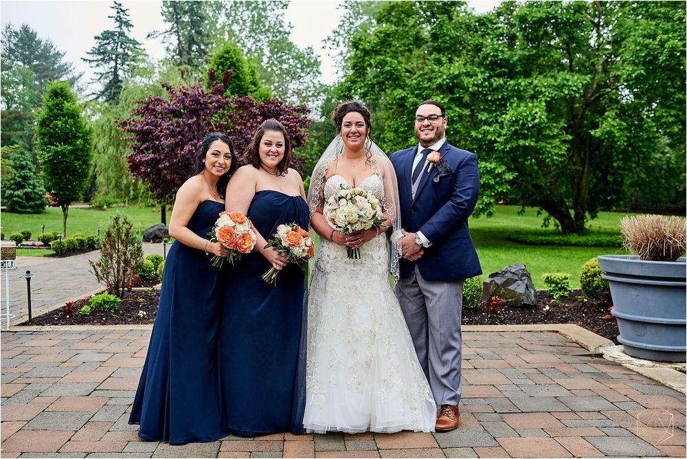 Small wedding party in navy blue and white poses on brick patio in garden setting.
