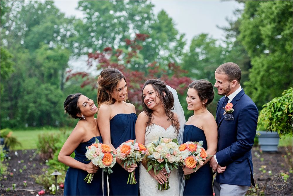 Wedding party in navy dresses holding coral and white bouquets poses together outdoors.