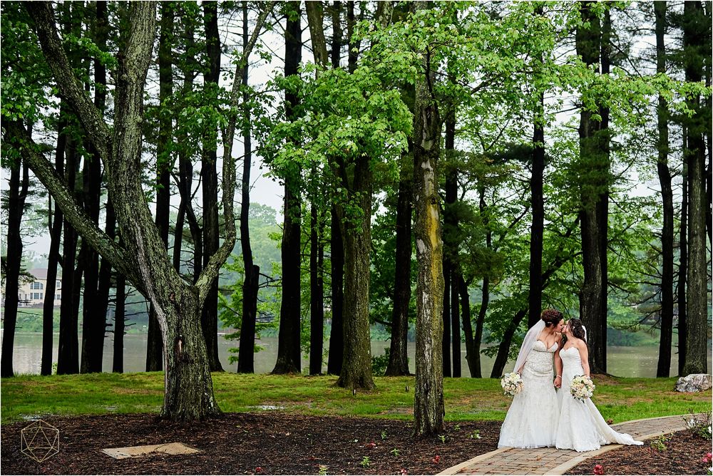 Two brides in white dresses walk together on a path through a lush green forest.