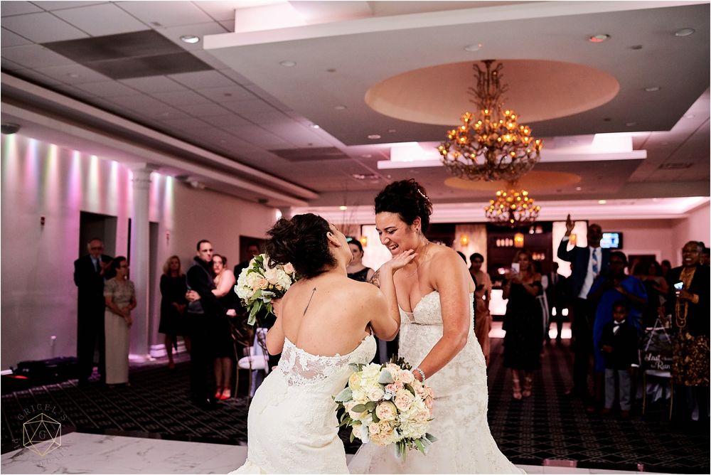 Wedding reception scene with brides dancing in an elegant ballroom with pink lighting.