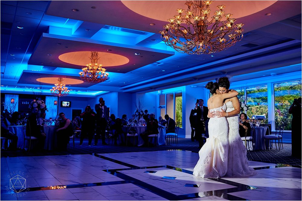 Couple sharing their first dance in a ballroom with dramatic blue lighting and chandeliers.