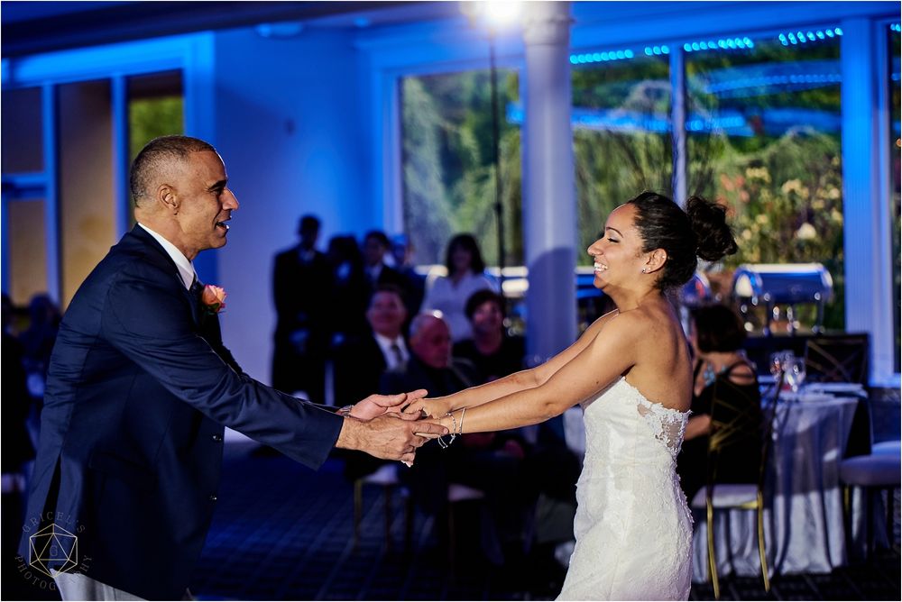 A couple dances together at their wedding reception in a room with blue uplighting and tropical artwork.