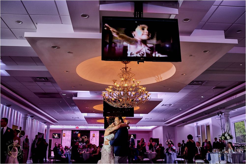 Wedding reception venue with overhead screens displaying the celebration under elegant chandeliers.