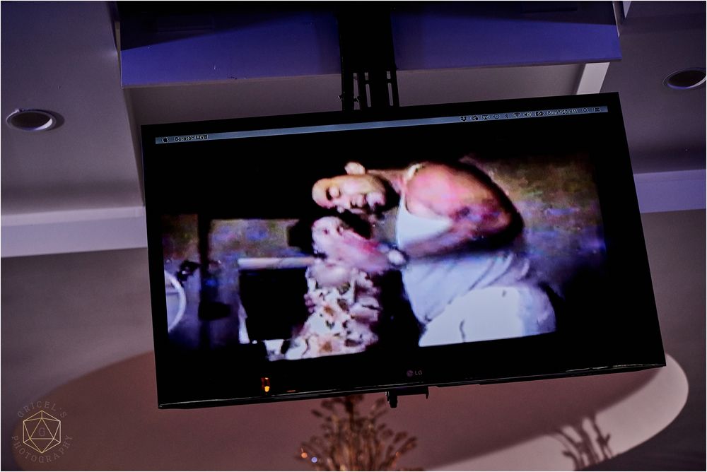 Large display screen showing wedding moments mounted on an elegant reception venue ceiling.